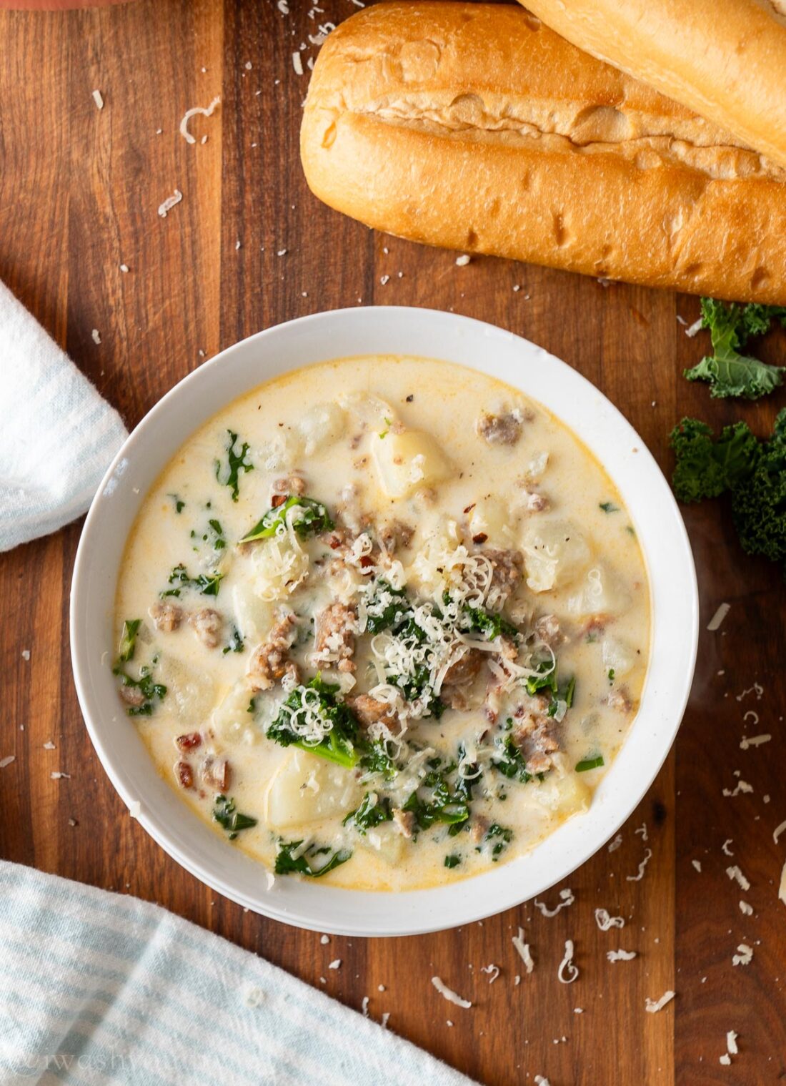 Bowl of zuppa toscana with breadsticks on wood cutting board. 