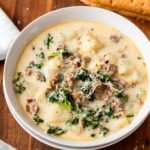 Bowl of zuppa toscana soup in white bowl on wood cutting board with breadstick.