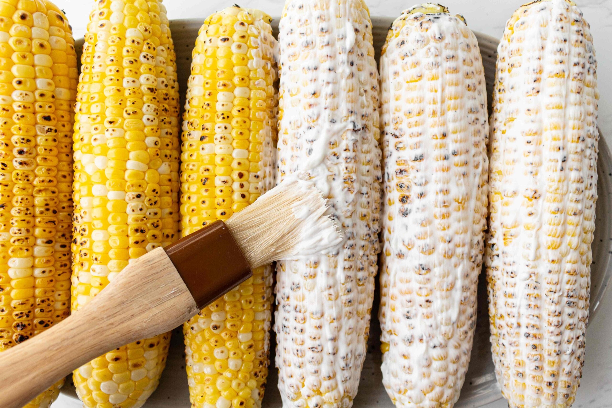 slathering creamy white sauce on grilled corn.