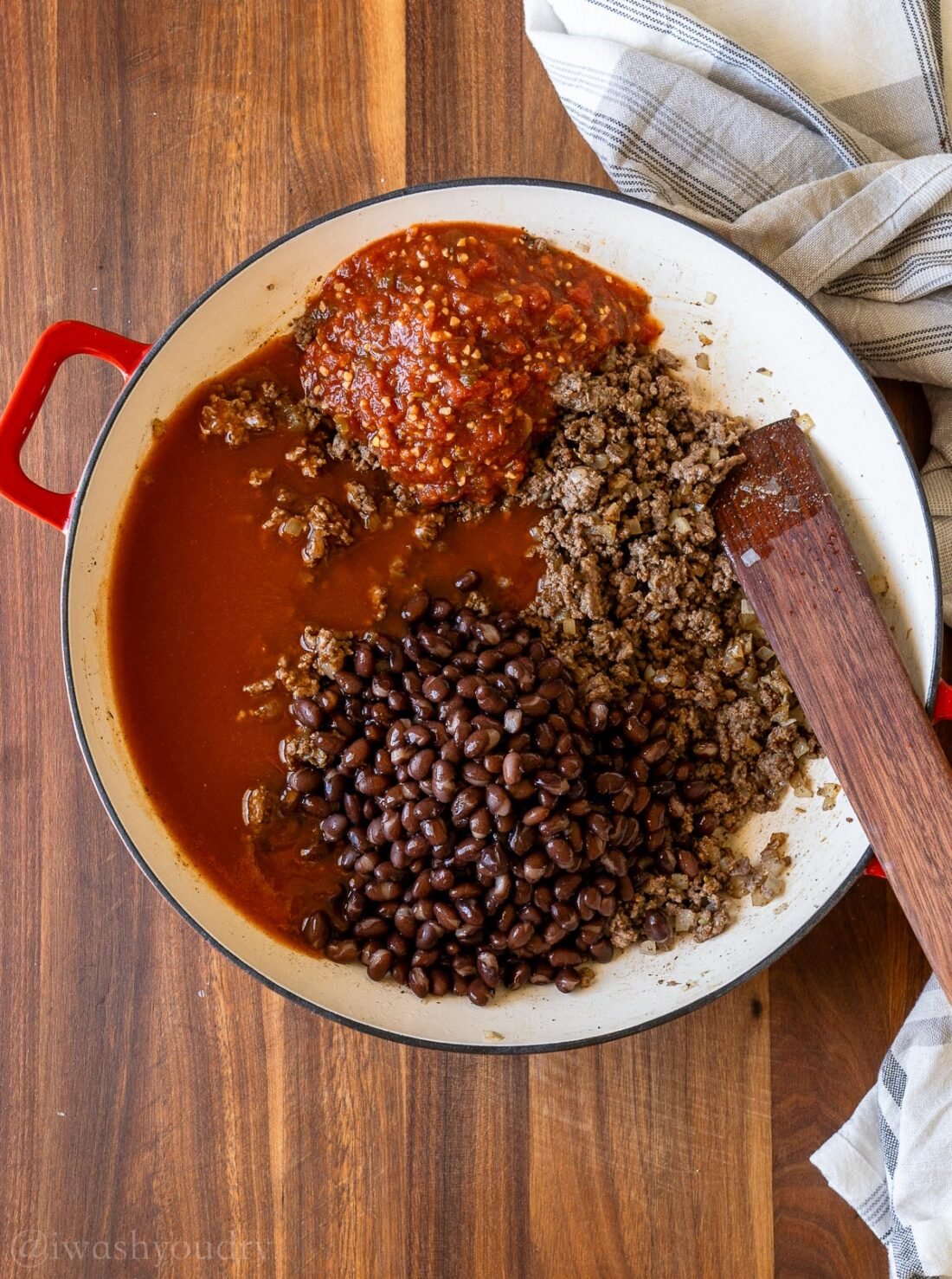 Skillet filled with sauces, black beans and ground beef with wooden spoon.