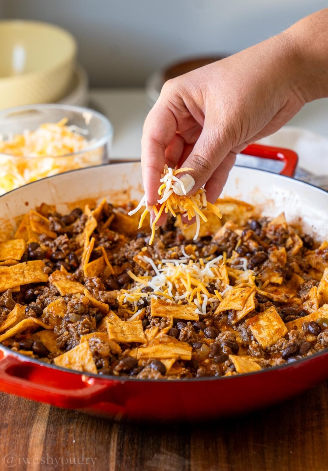 sprinkling cheese on top of enchilada casserole with beef and beans.