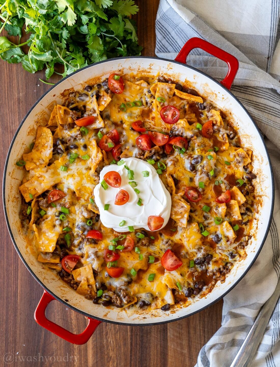 cheesy ground beef enchilada casserole in skillet, topped with sour cream and diced tomatoes.