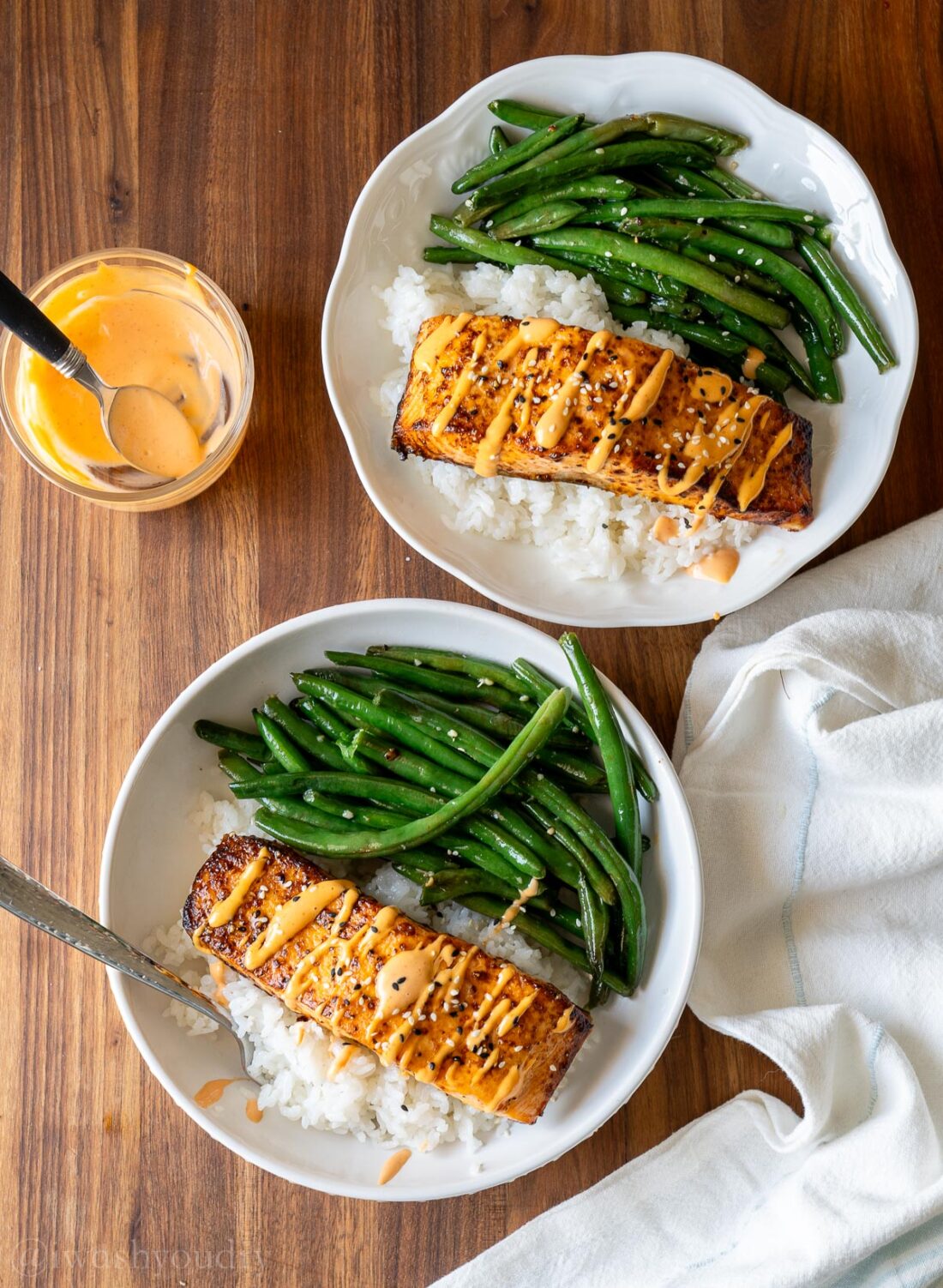 two bowls on a wooden surface, filled with salmon and green beans.