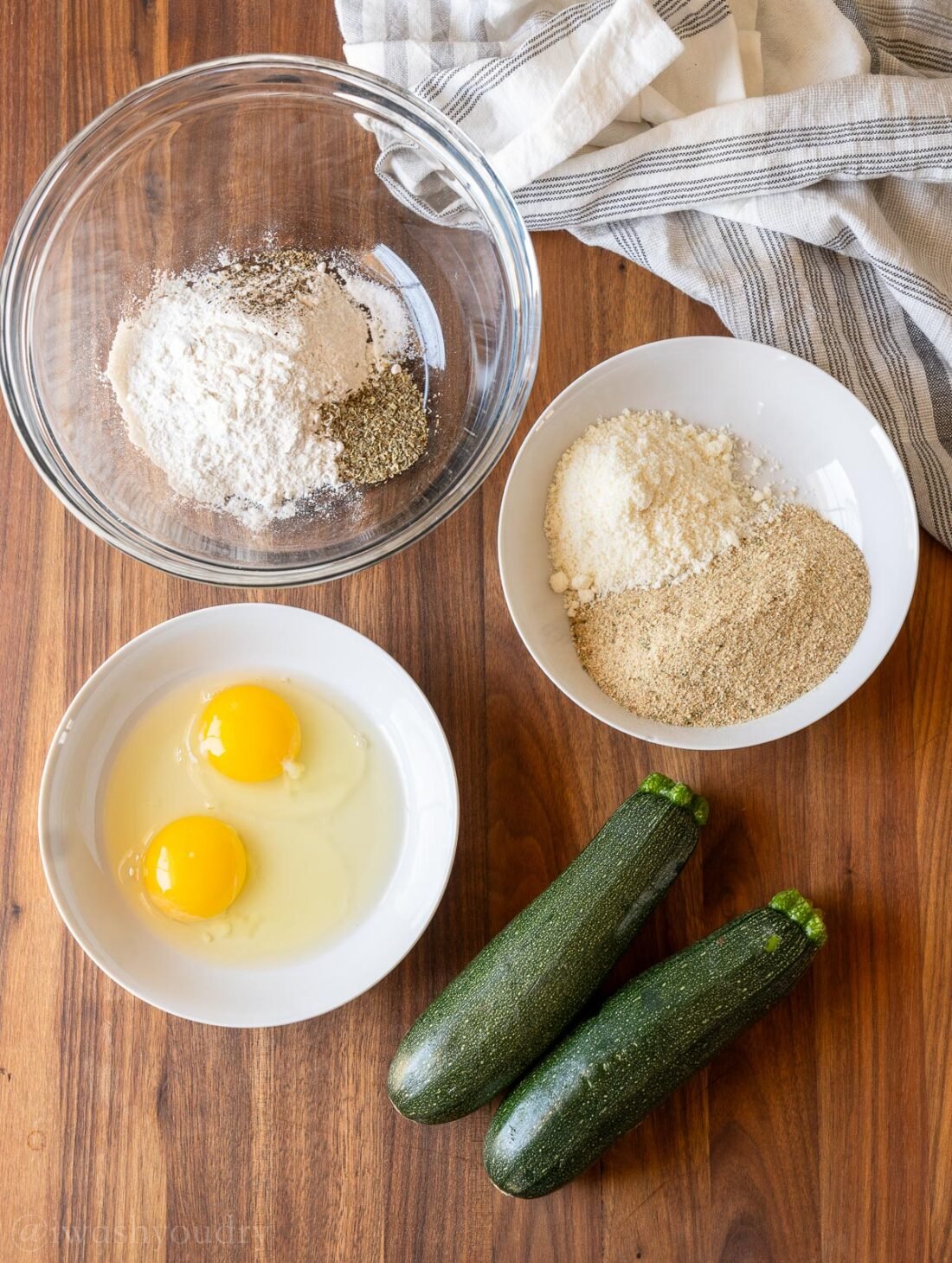 Ingredients for zucchini fries on wooden surface with eggs and flour.