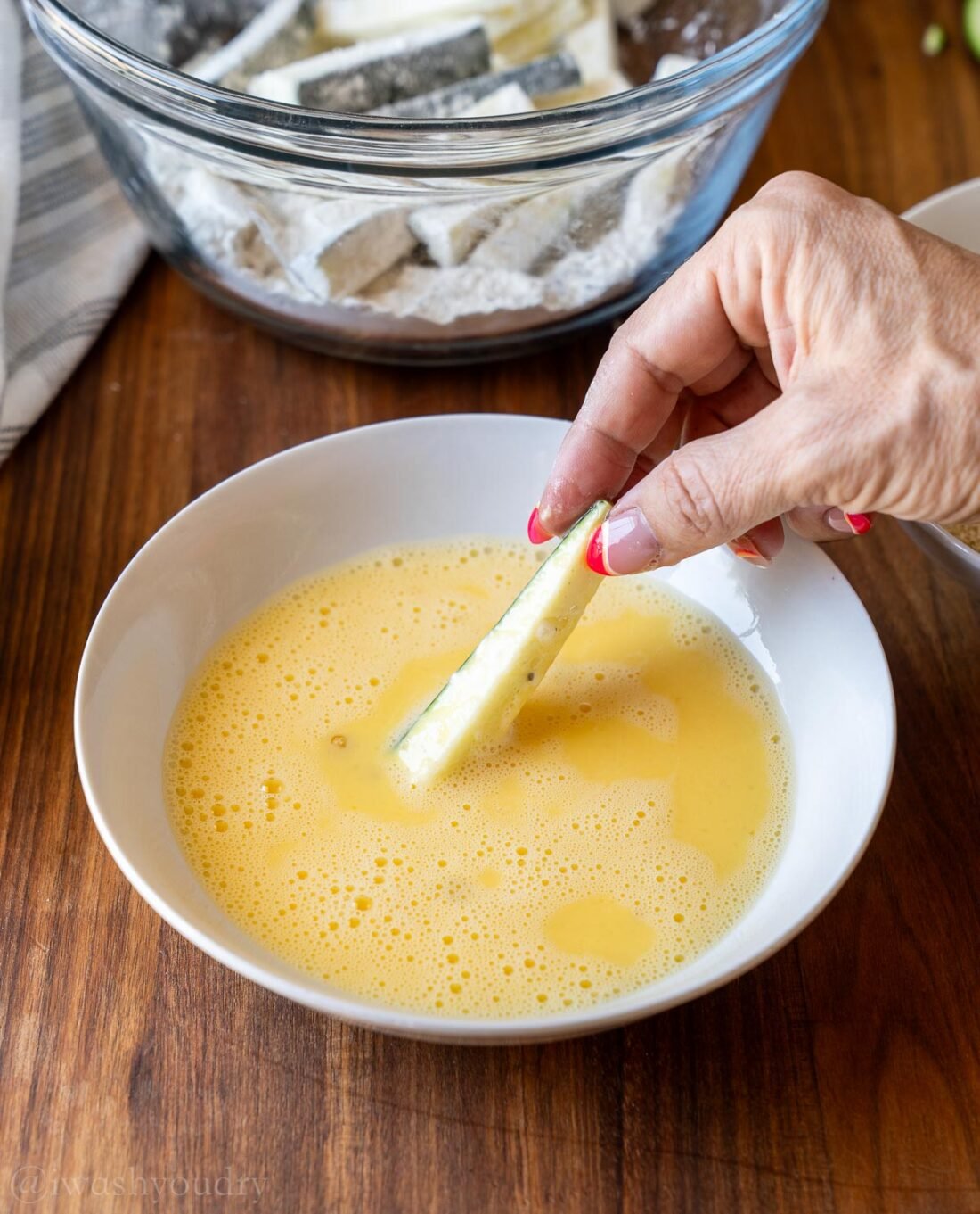 dipping zucchini fries in egg batter in white bowl.