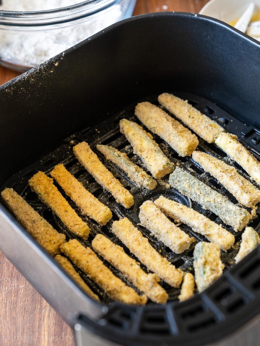 uncooked zucchini fries in air fryer basket.