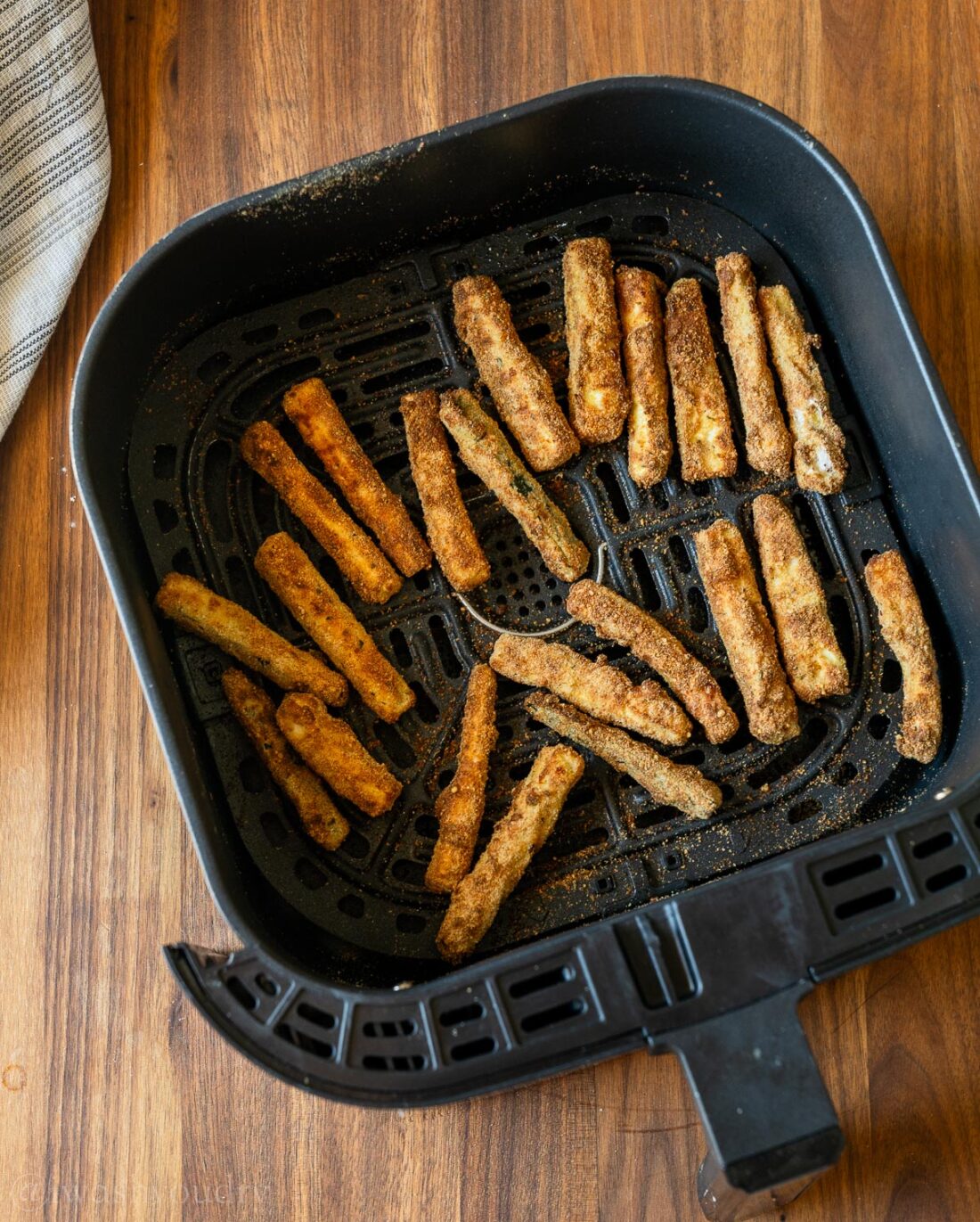 cooked zucchini fries in air fryer basket.