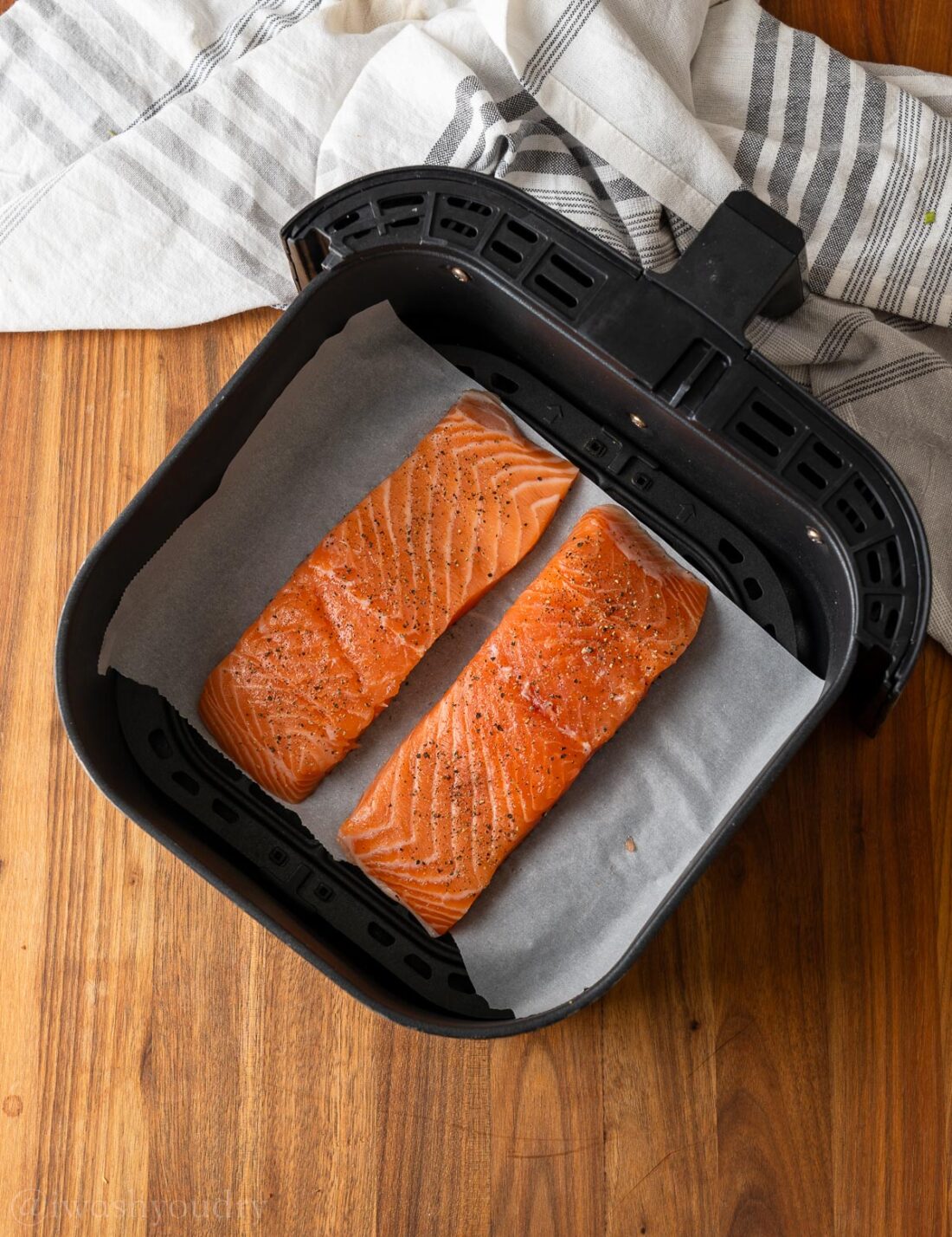 raw salmon in air fryer basket on parchment paper.