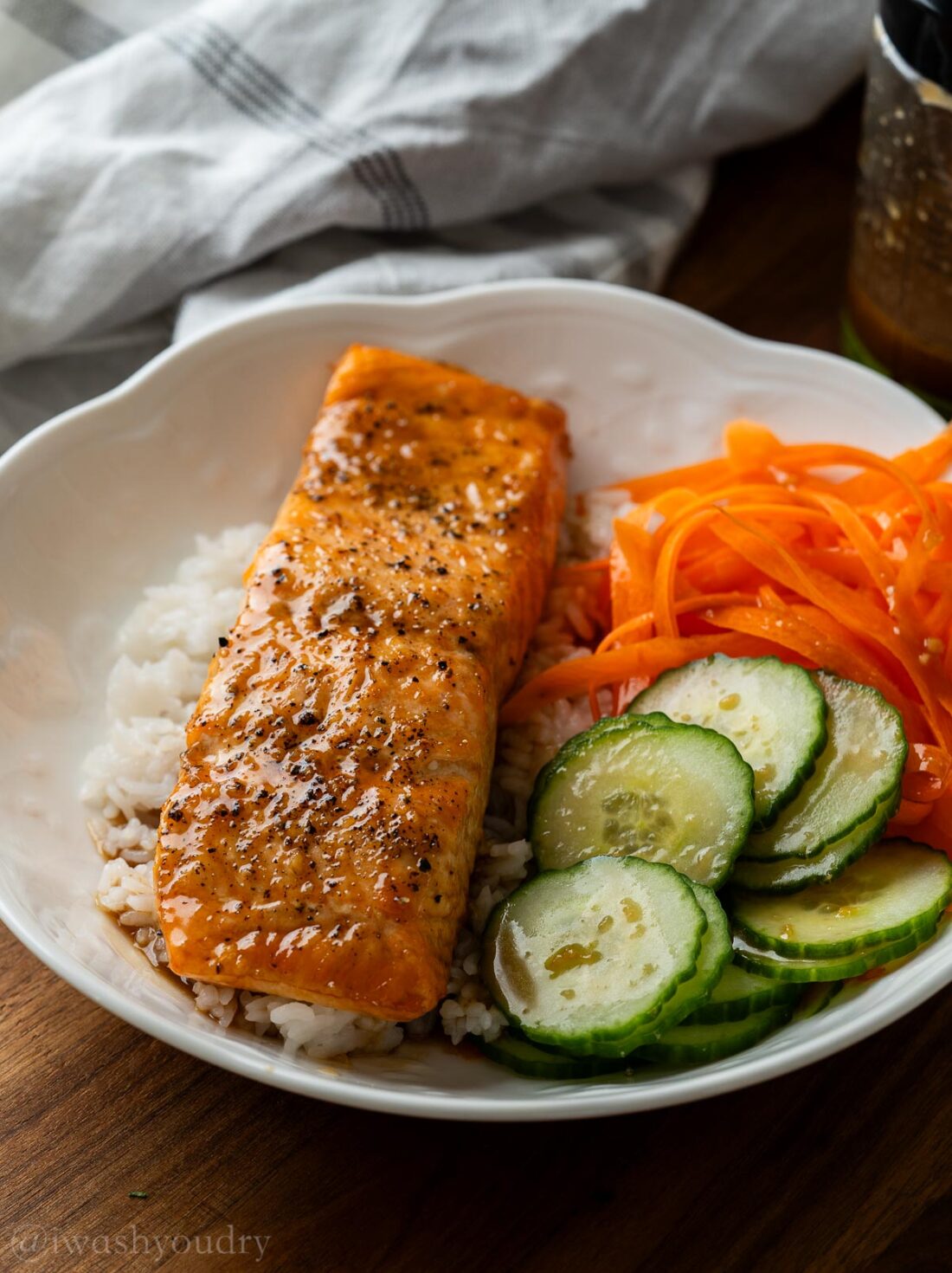 salmon filet in white bowl with cucumbers and carrots.