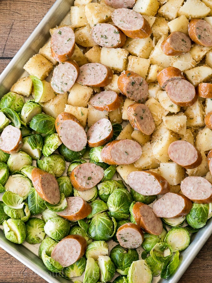 uncooked potatoes, brussels sprouts and sausages on a sheet pan.