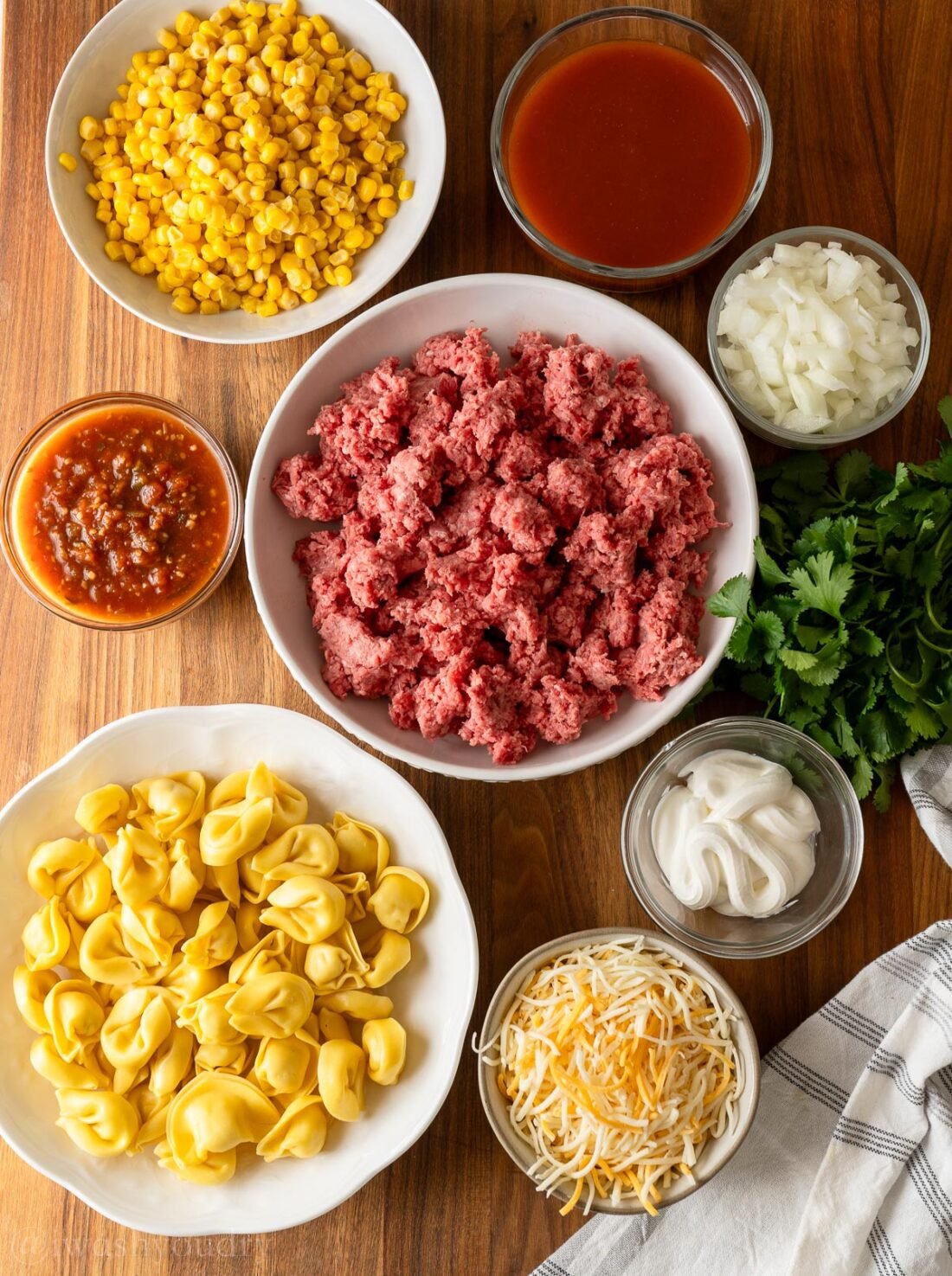 ingredients for tortellini and beef enchiladas on wooden surface.