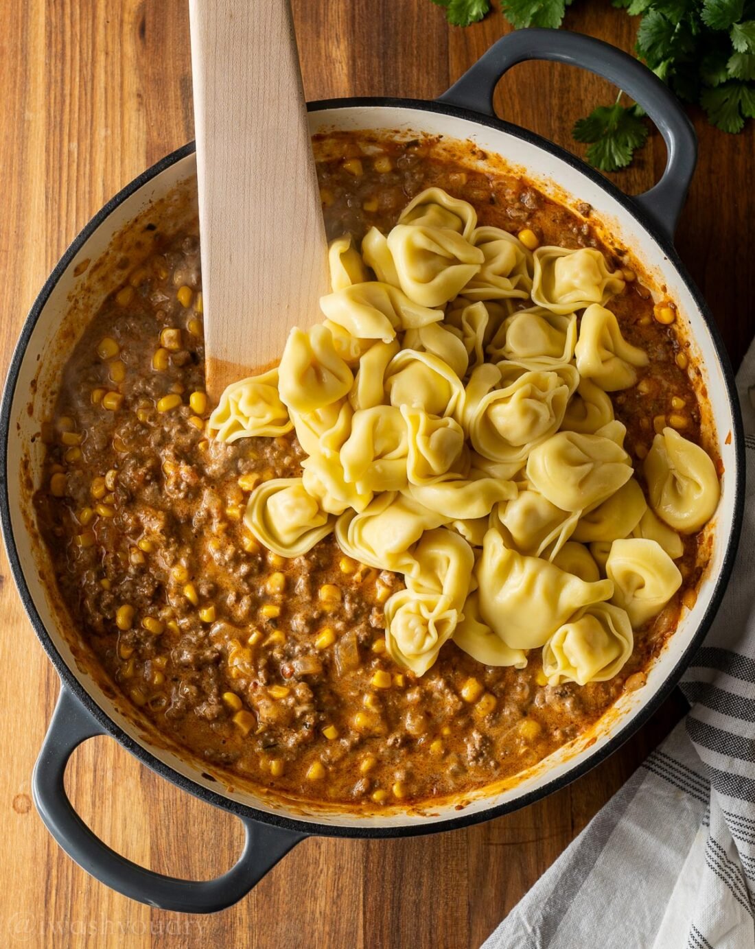 cheesy beef enchilada tortellini in skillet with wooden spoon.