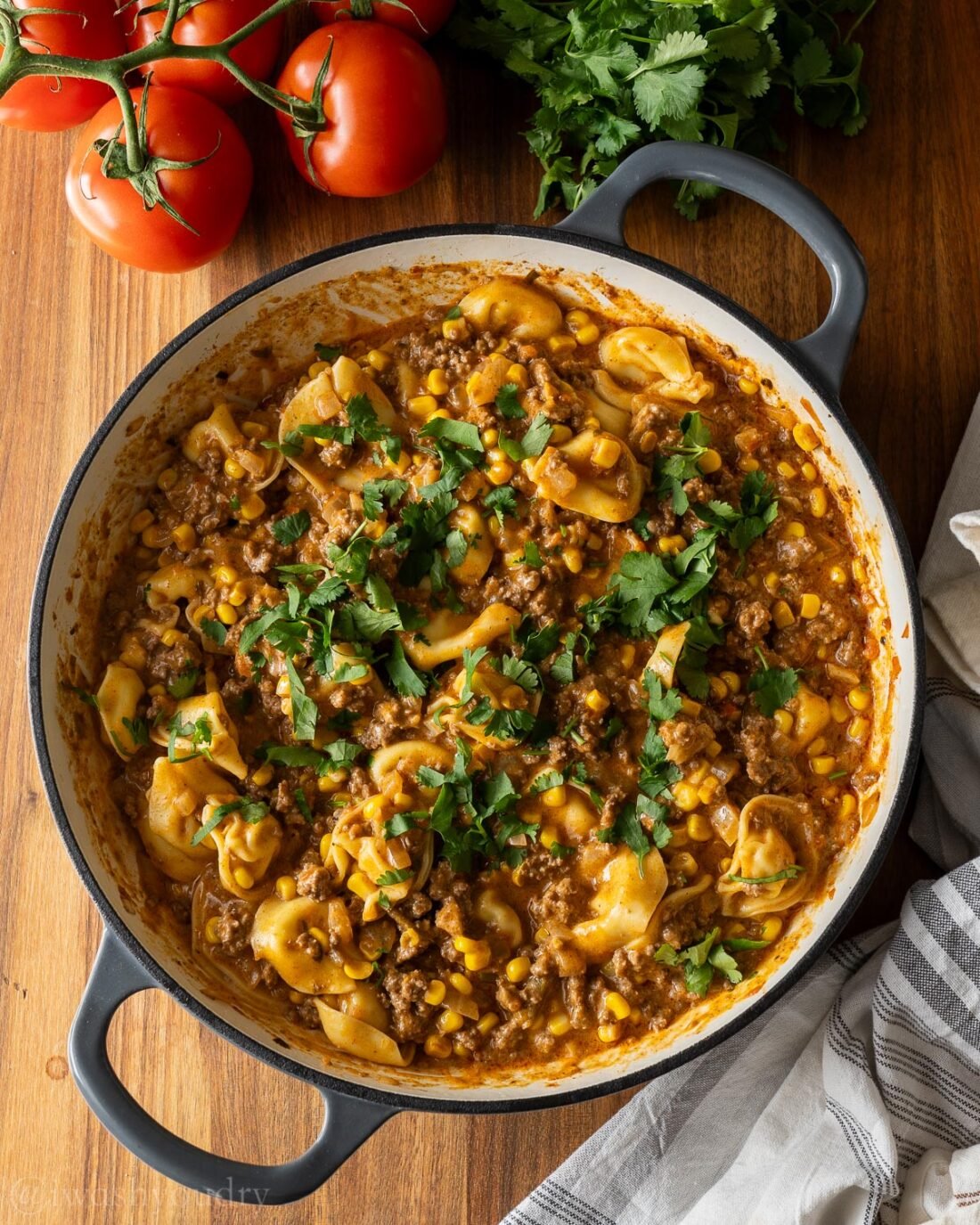 tortellini and ground beef in skillet with enchilada sauce and cilantro on top.