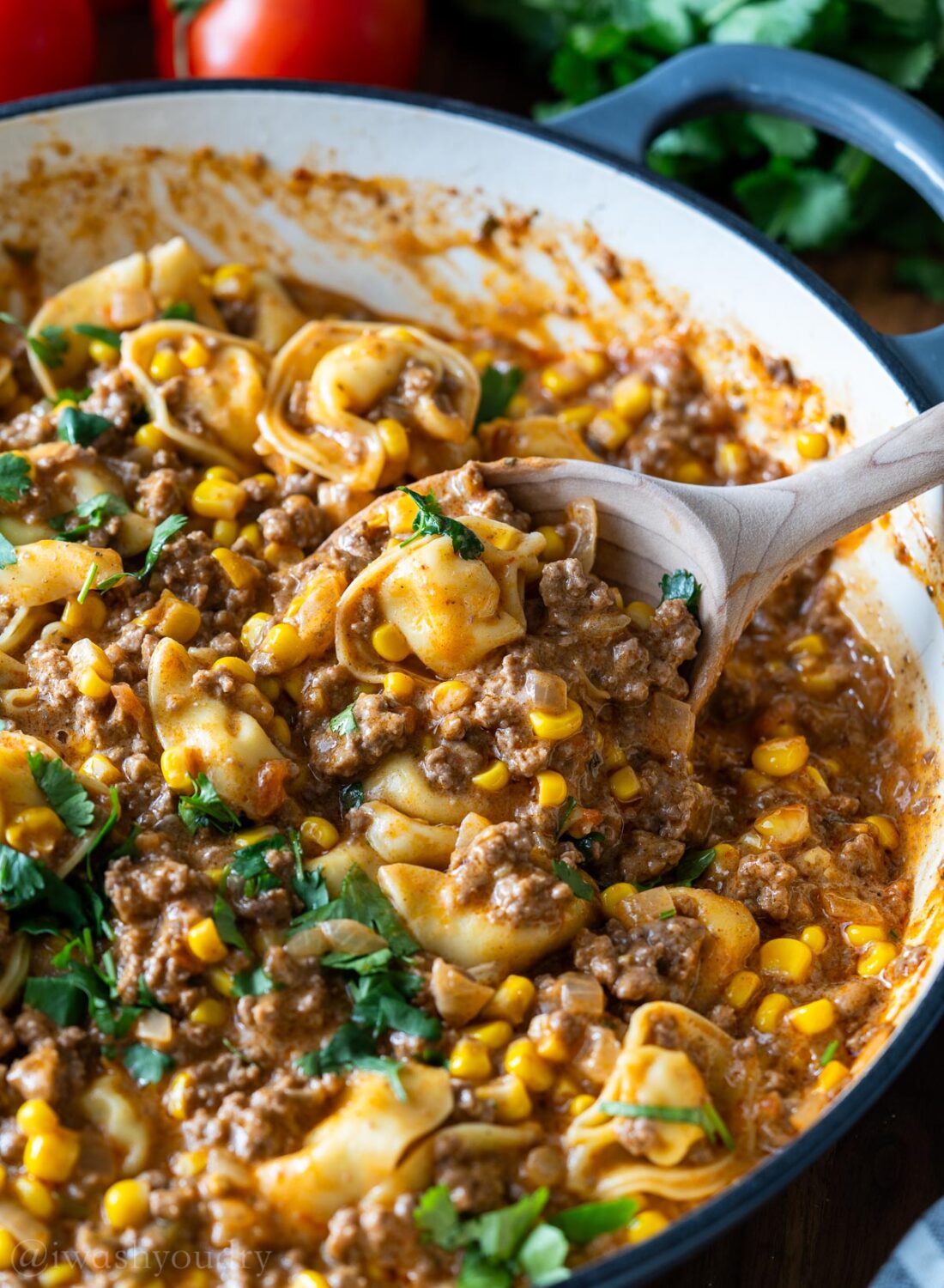 skillet filled with ground beef, tortellini and corn with spoon inside.