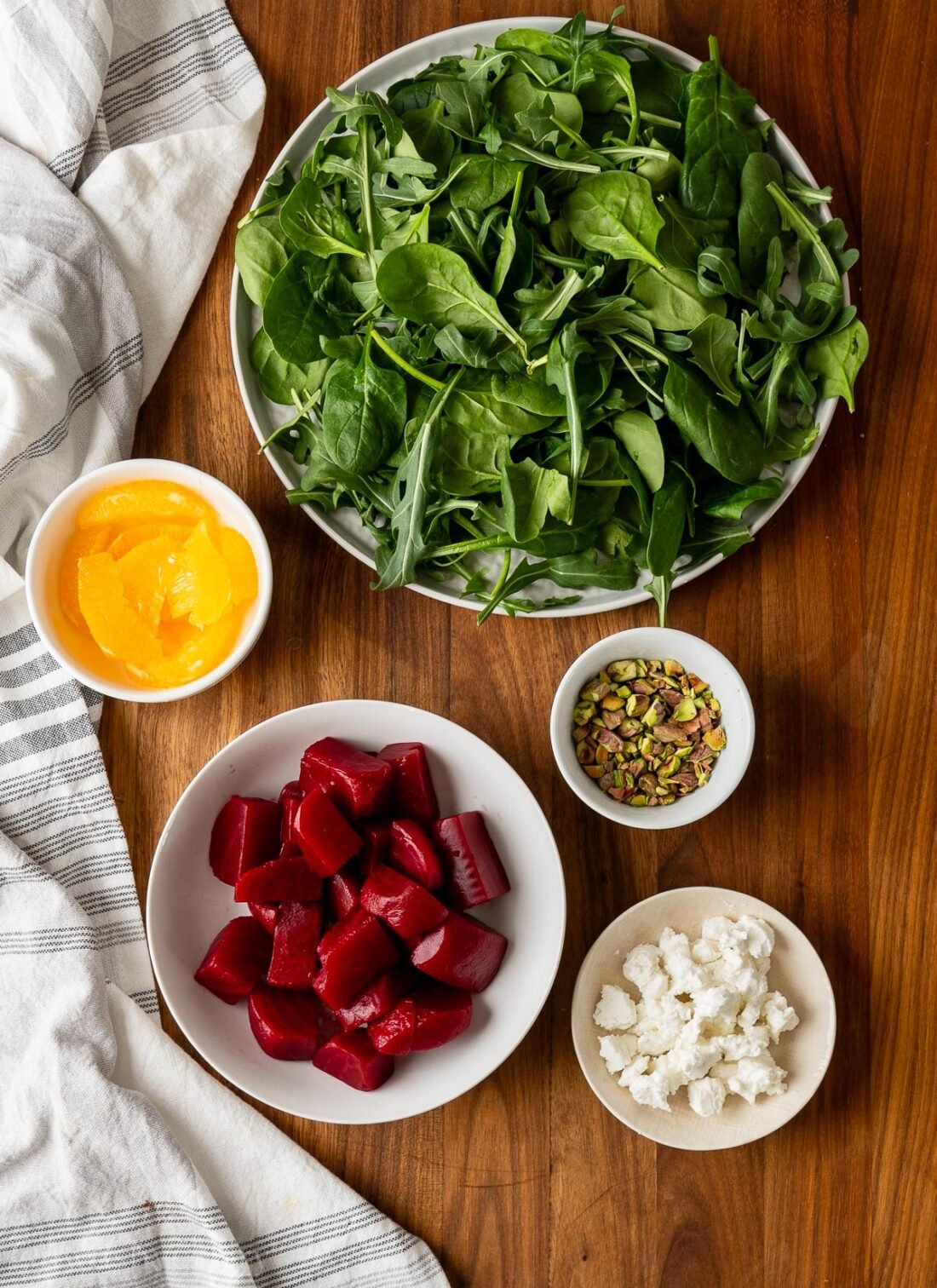 cut beets in white bowl with platter of spinach and arugula next to it.