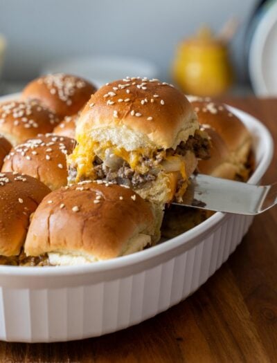 cheeseburger slider being pulled out of a casserole dish with sesame seeds on top.