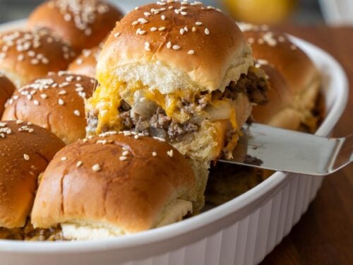 cheeseburger slider being pulled out of a casserole dish with sesame seeds on top.