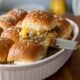 cheeseburger slider being pulled out of a casserole dish with sesame seeds on top.