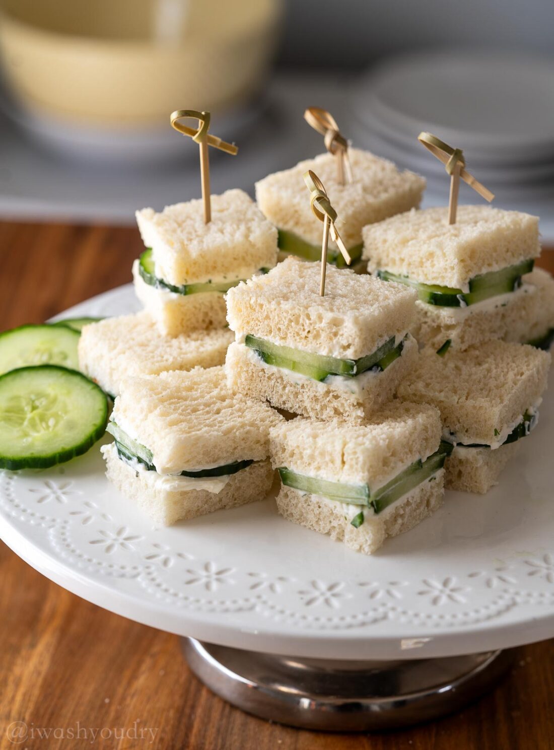 stacked cucumber sandwiches on platter with toothpicks inserted in center.