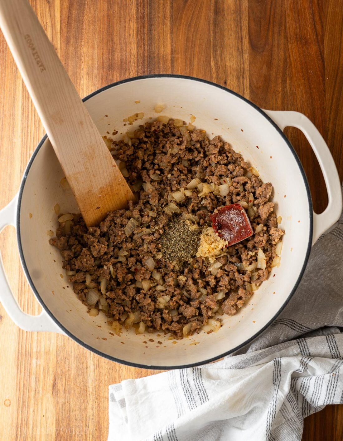 browned sausage in dutch oven with wooden spoon.