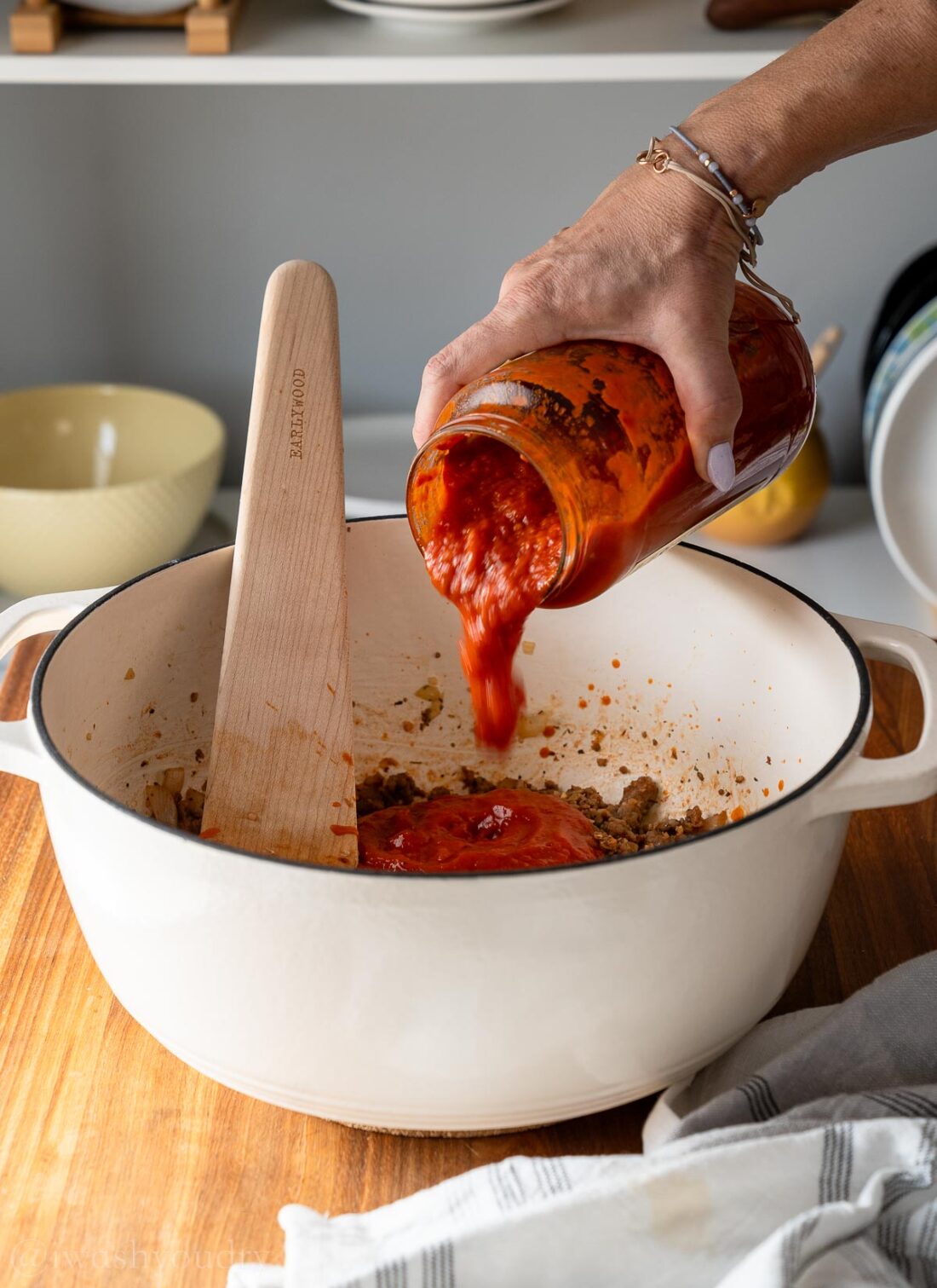 adding in marinara sauce to white pot with wooden spoon.