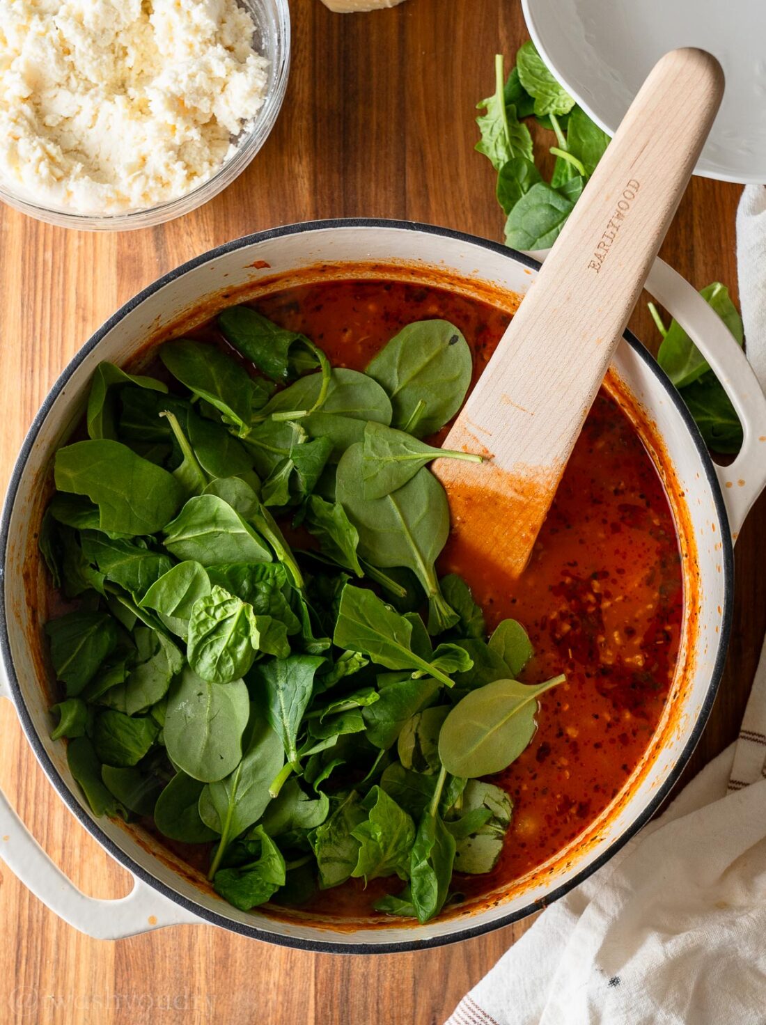 baby spinach in pot of soup with tomatoes.