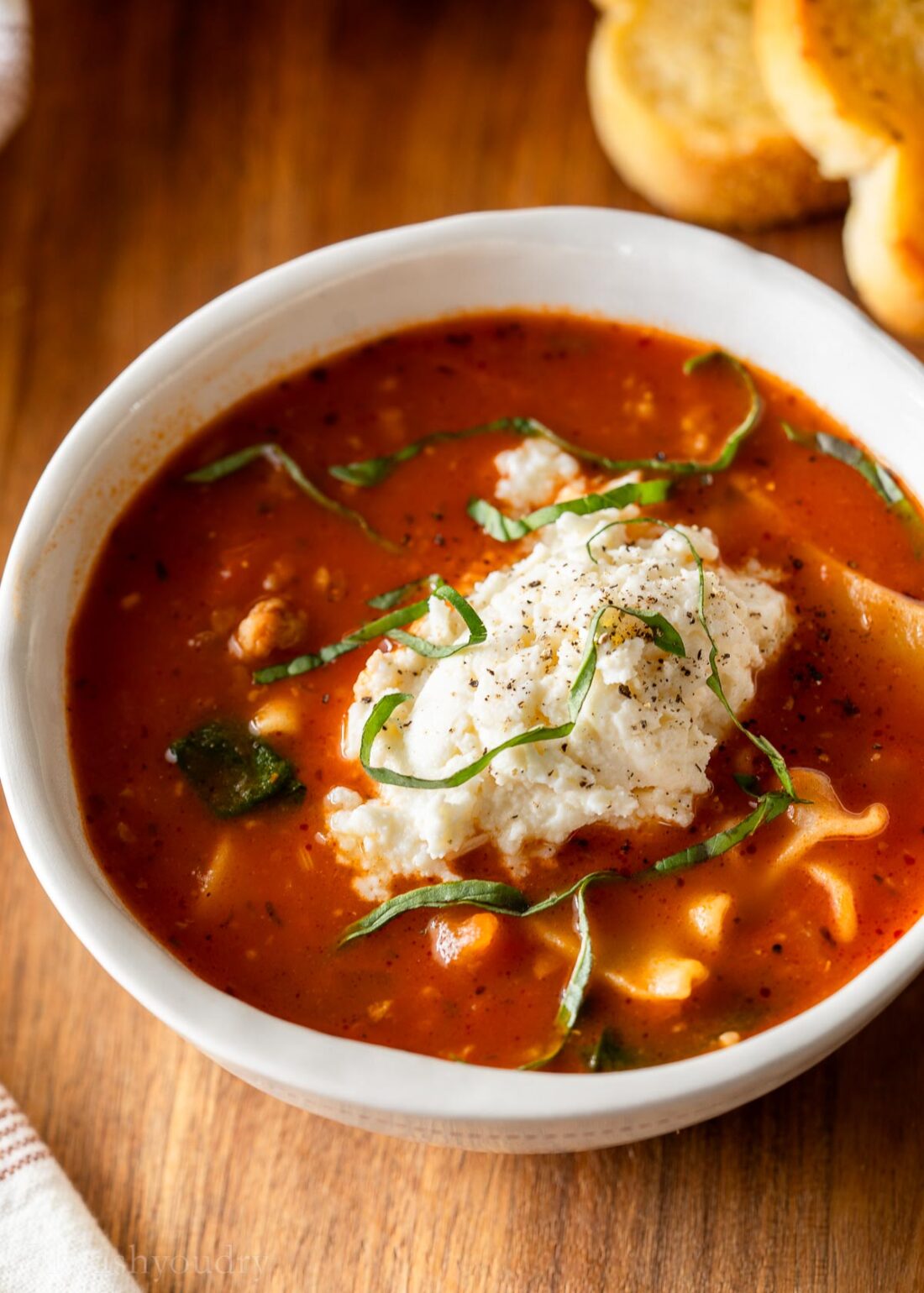 bowl of lasagna soup with ricotta cheese dumpling on top.