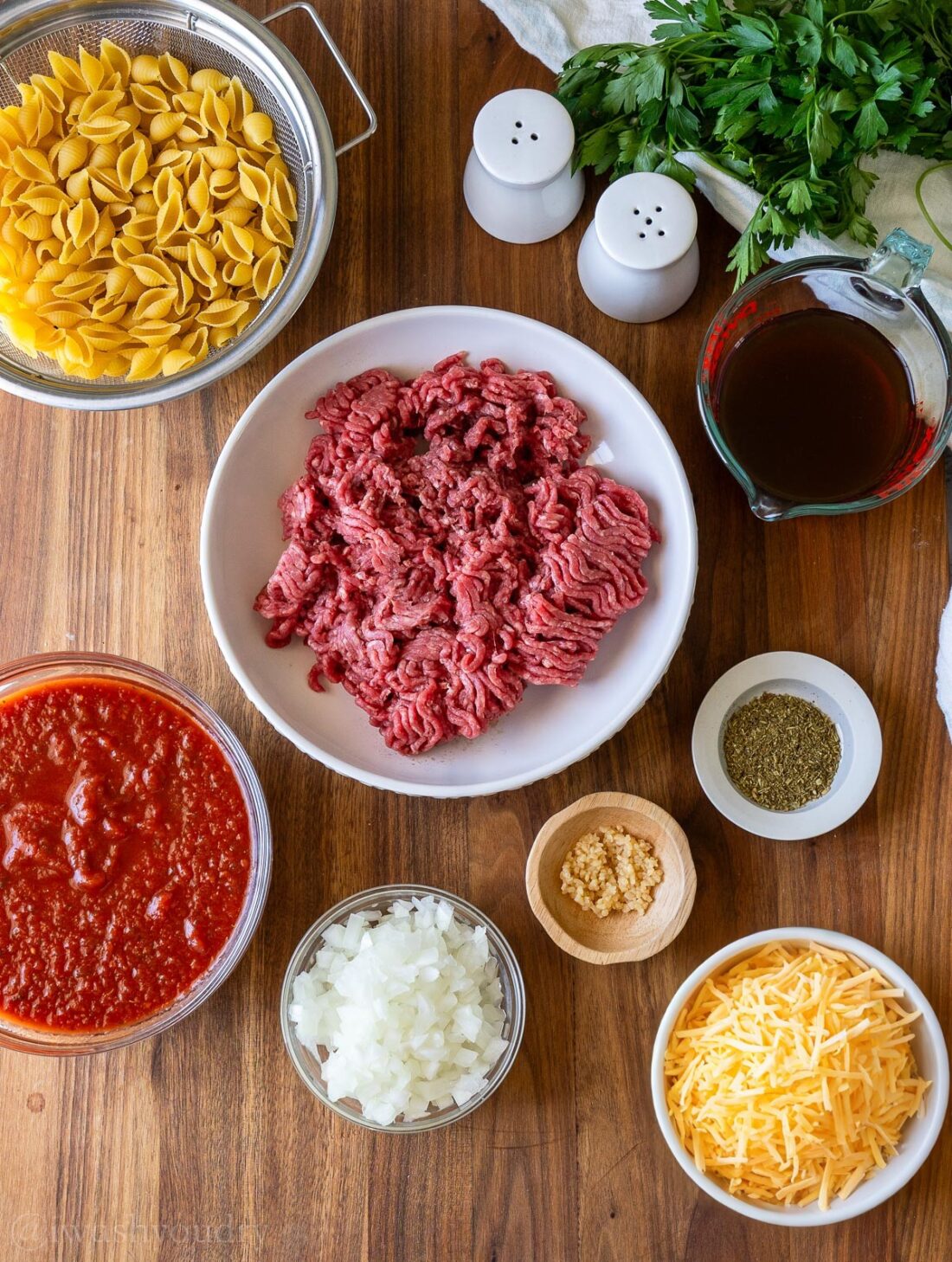 ingredients for ground beef helper on wooden surface with cheese and pasta shells.
