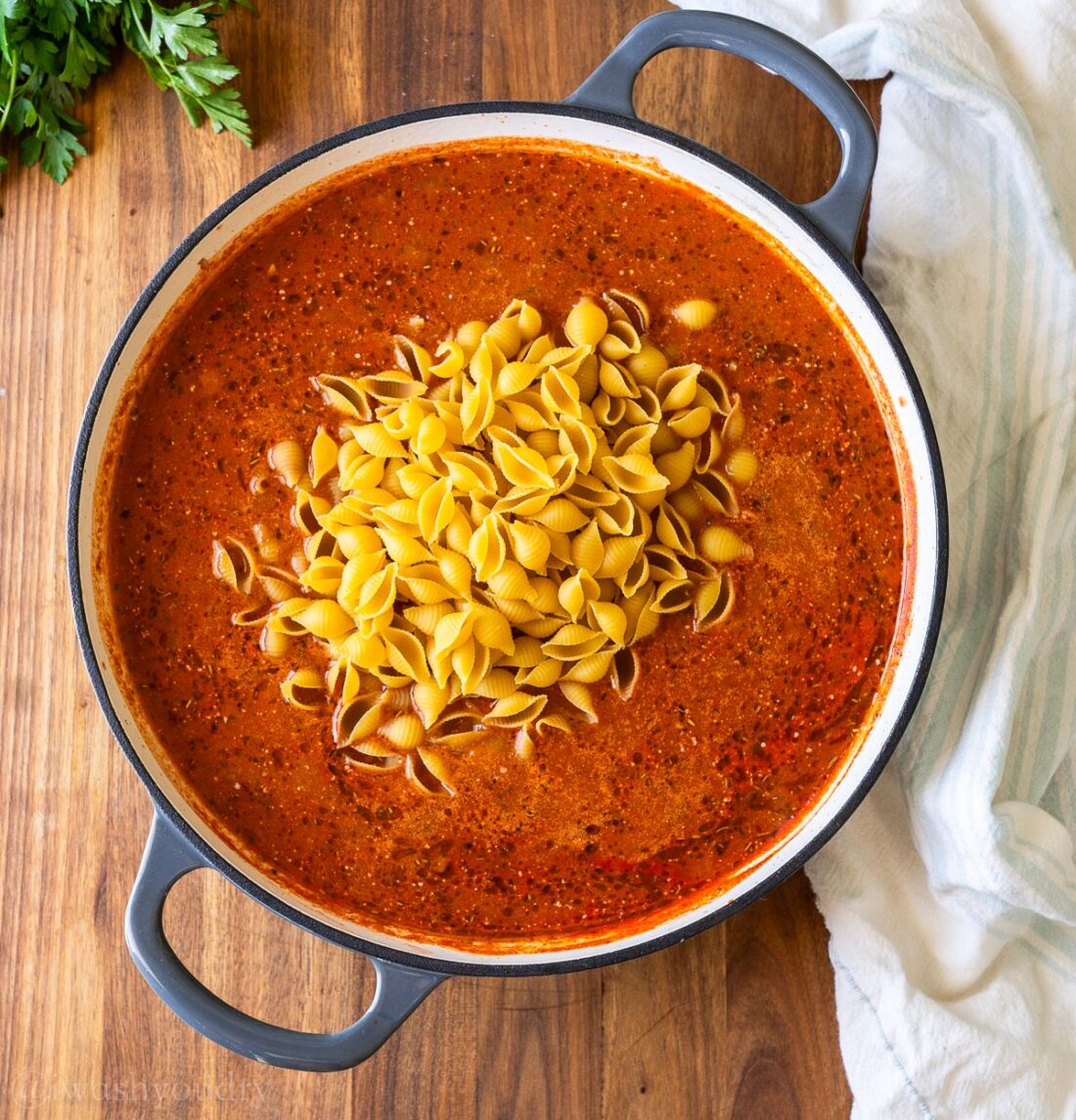 pasta sauce with uncooked pasta shells in large skillet with gray handles.