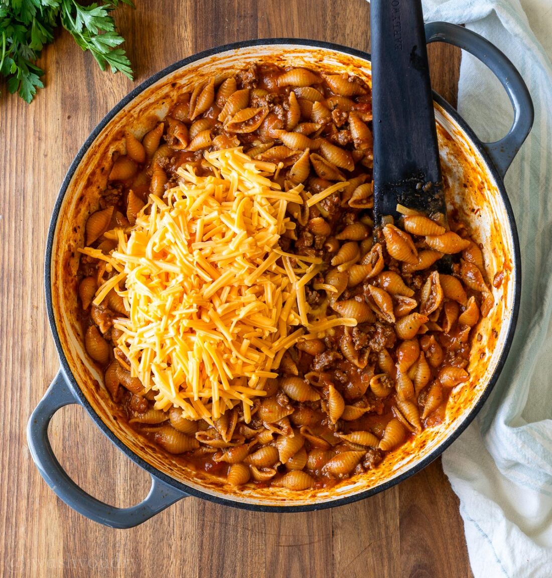 cooked pasta shells in red sauce with a pile of cheddar cheese ready to be stirred in.