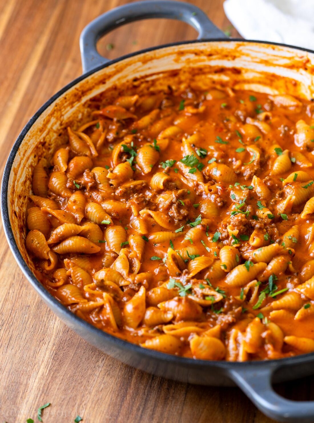 gray skillet filled with cheesy hamburger helper recipe and ground beef in a tomato based sauce.