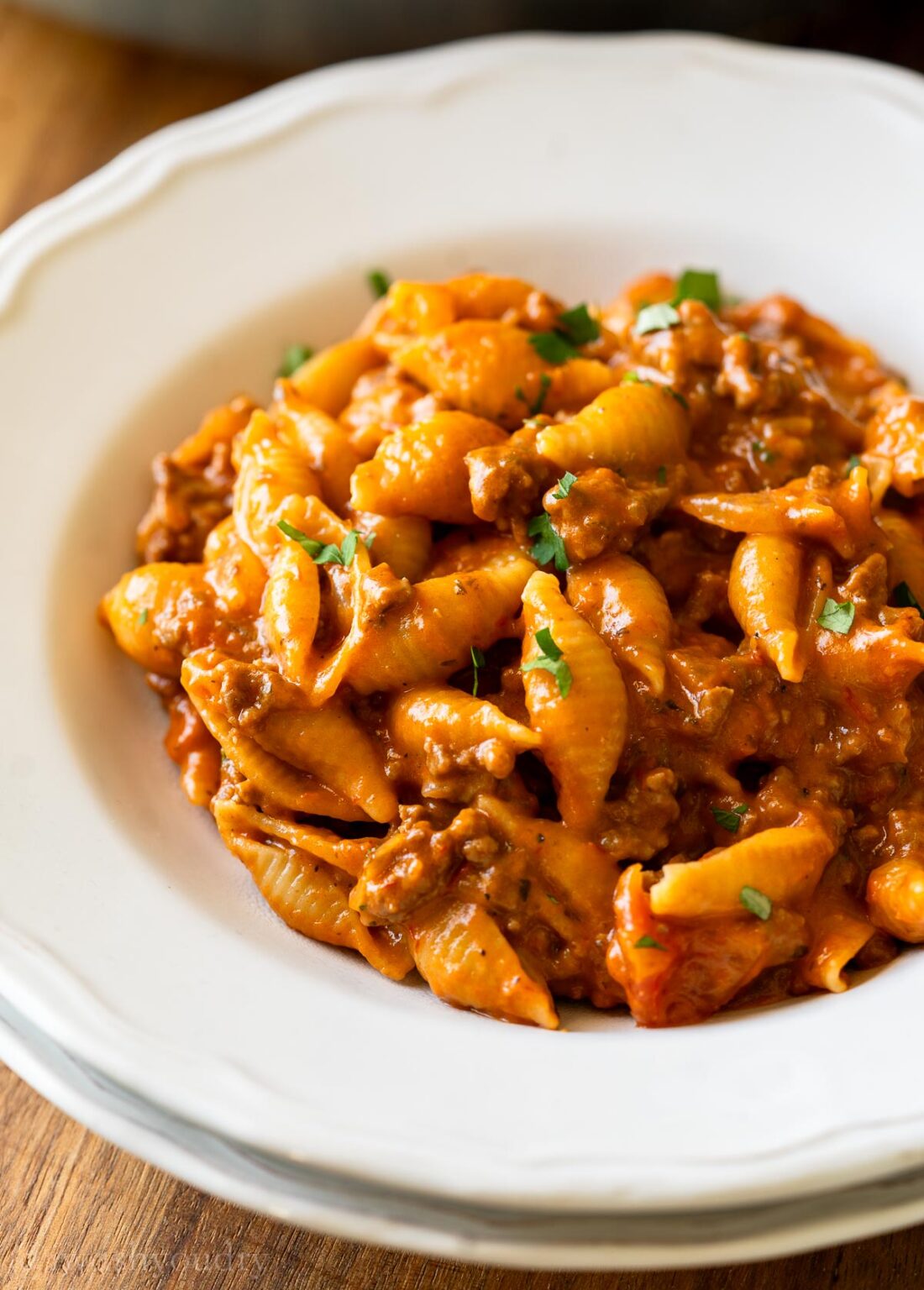 white bowl filled with hamburger helper recipe in a creamy tomato sauce with parsley on top.