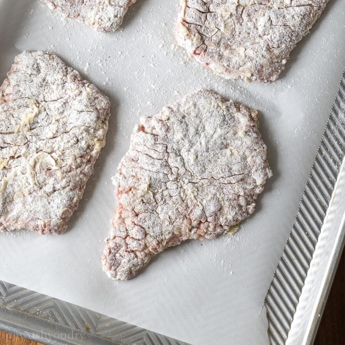 breaded steaks coated in flour on parchment paper ready to fry.