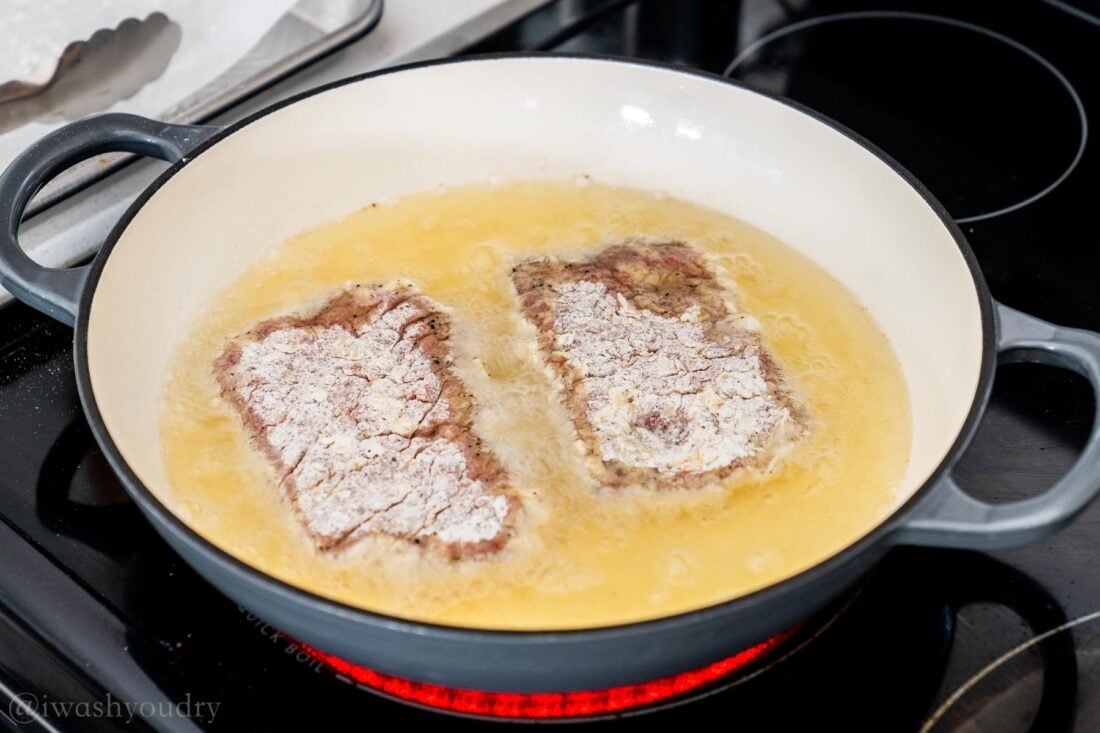 frying country steaks in oil on stove top.