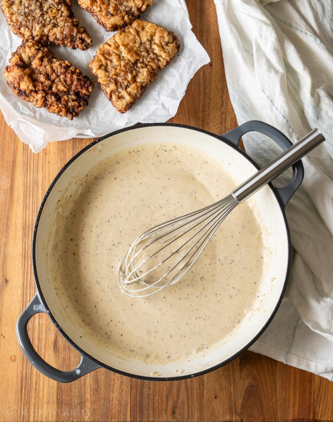 white gravy with pepper in a pan with country fried steaks on a plate beside it.