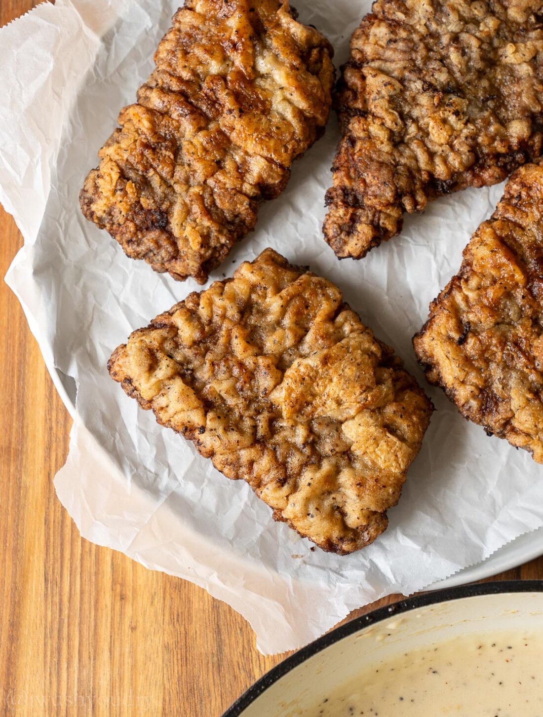 chicken fried steaks on parchment paper lined plate.