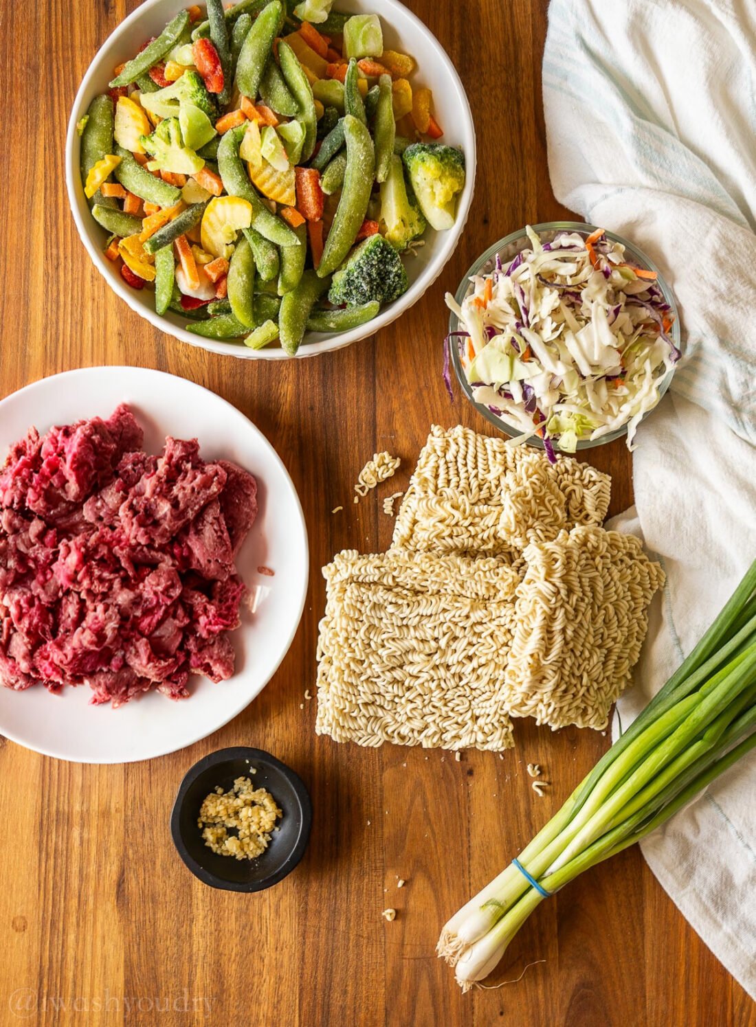 ingredients for ramen stir fry on wooden surface with ground beef and green onions.
