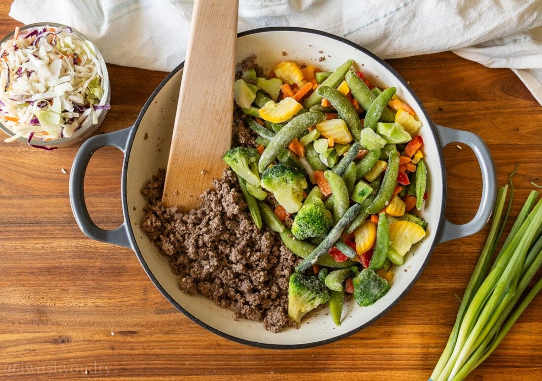 skillet with ground beef on one side and frozen veggies on the other.