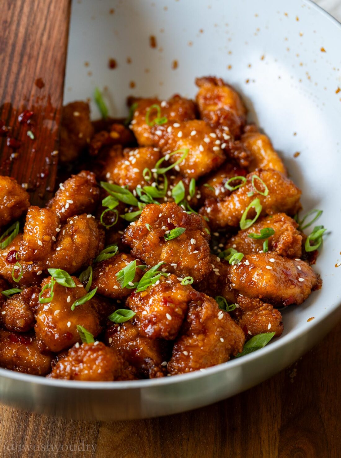 wok full of sweet chili chicken topped with green onions and sesame seeds.