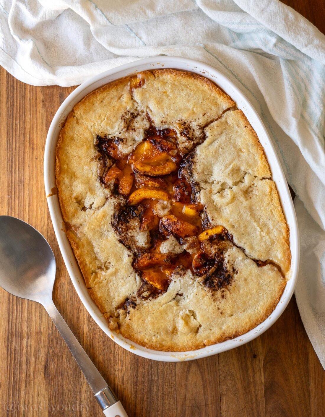 Baking dish with old fashioned peach cobbler and serving spoon next to it.