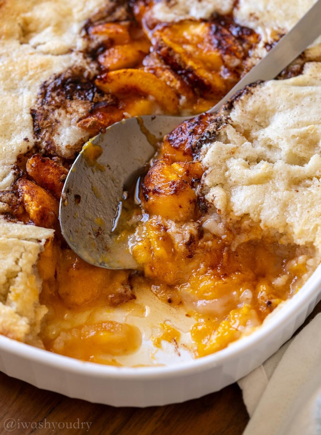 baked peach cobbler with spoon inside dish.