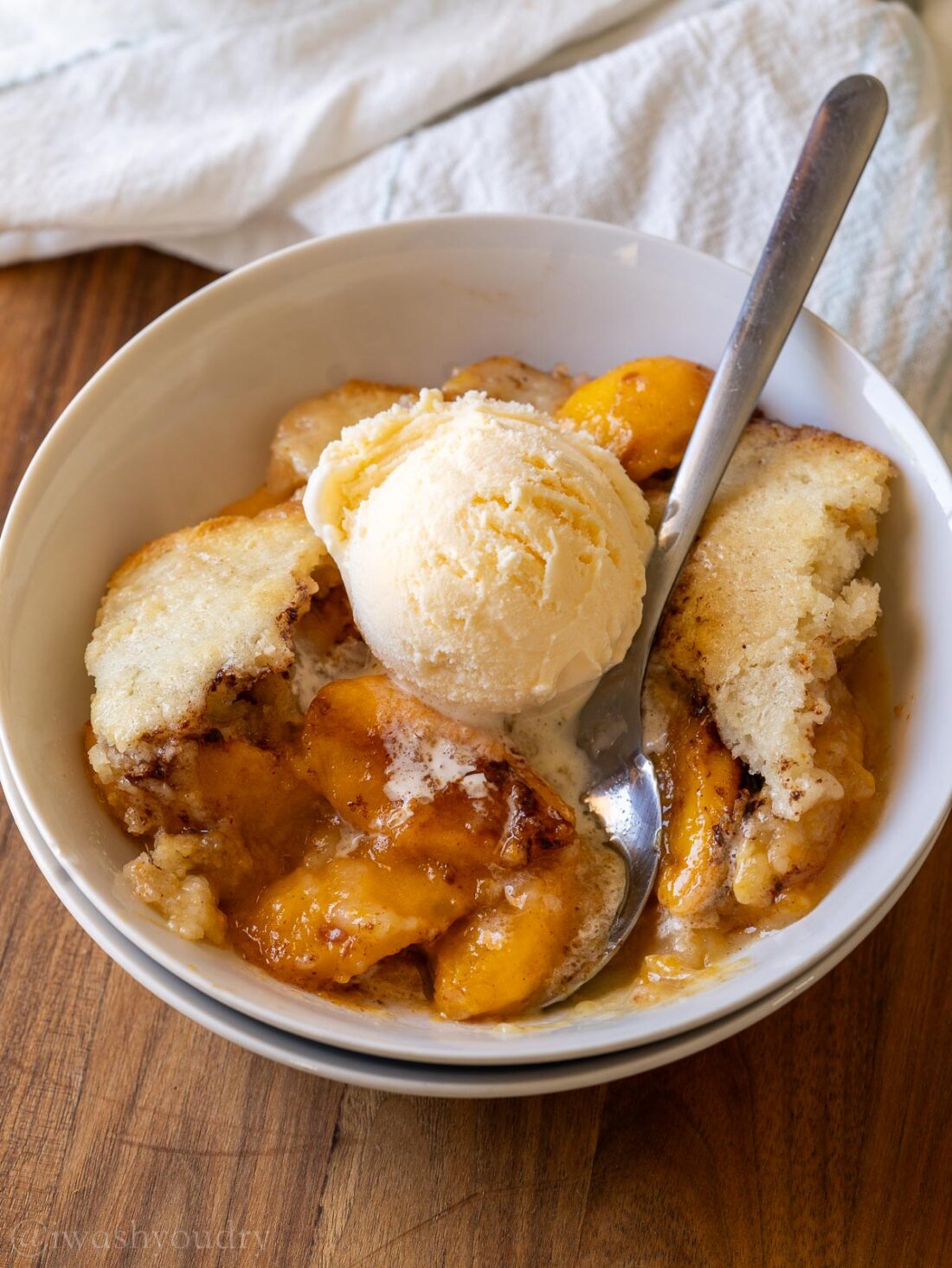 bowl filled with fresh peach cobbler with a scoop of vanilla ice cream on top. 