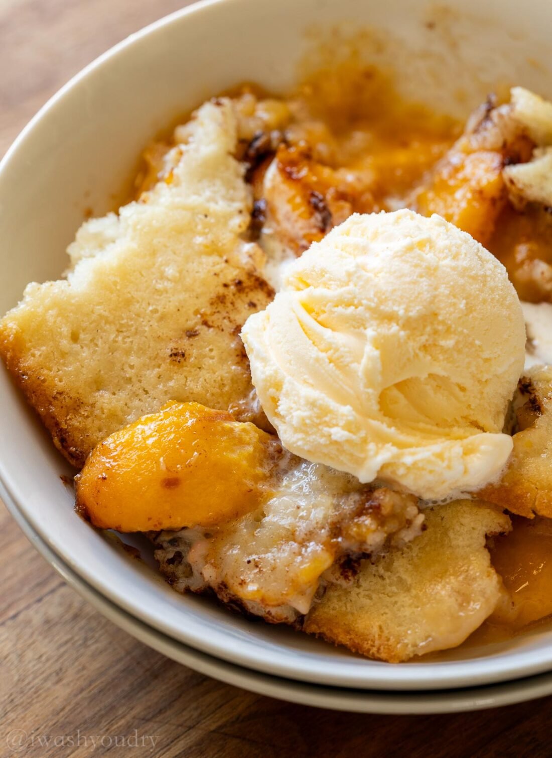 peach cobbler in bowl with a scoop of vanilla ice cream on top.