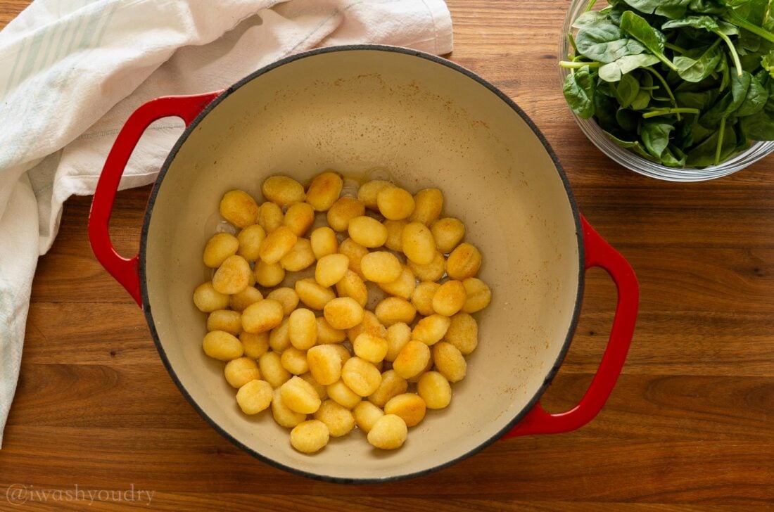 toasted gnocchi in a red pot with spinach in a bowl next to it.