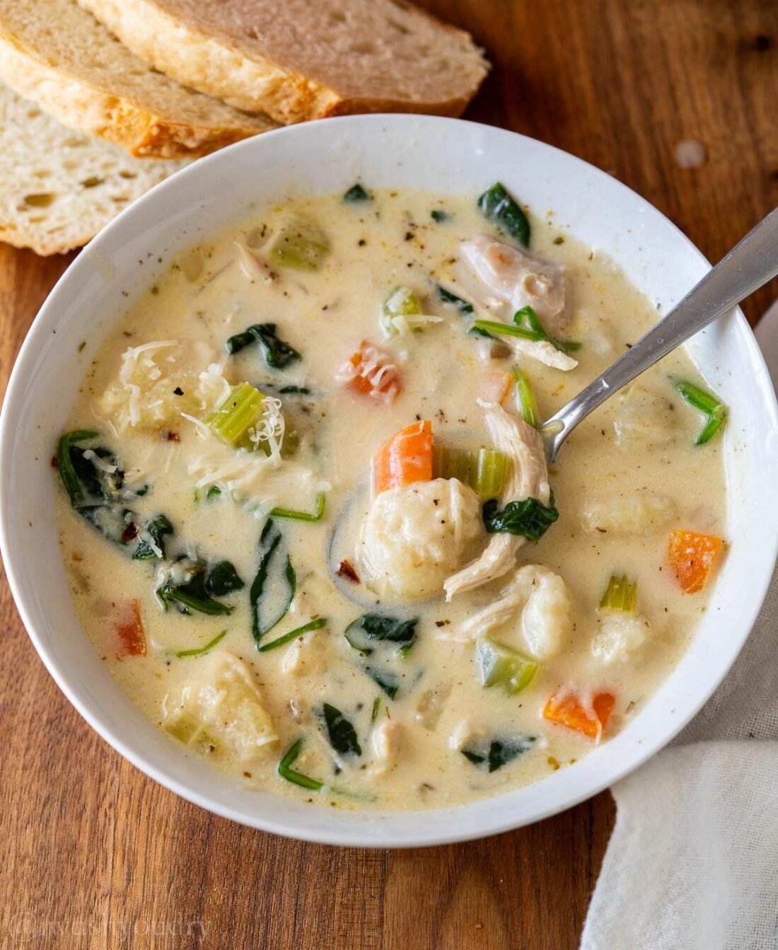 creamy soup with carrots, gnocchi and chicken in a white bowl with spoon inside.