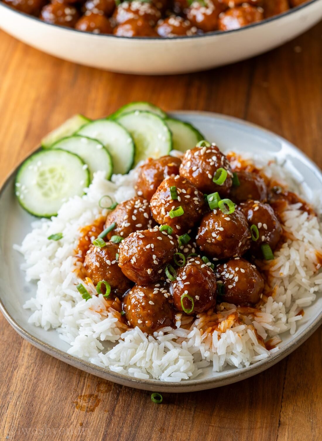 plate with korean bbq meatballs over rice with cucumbers on the side.