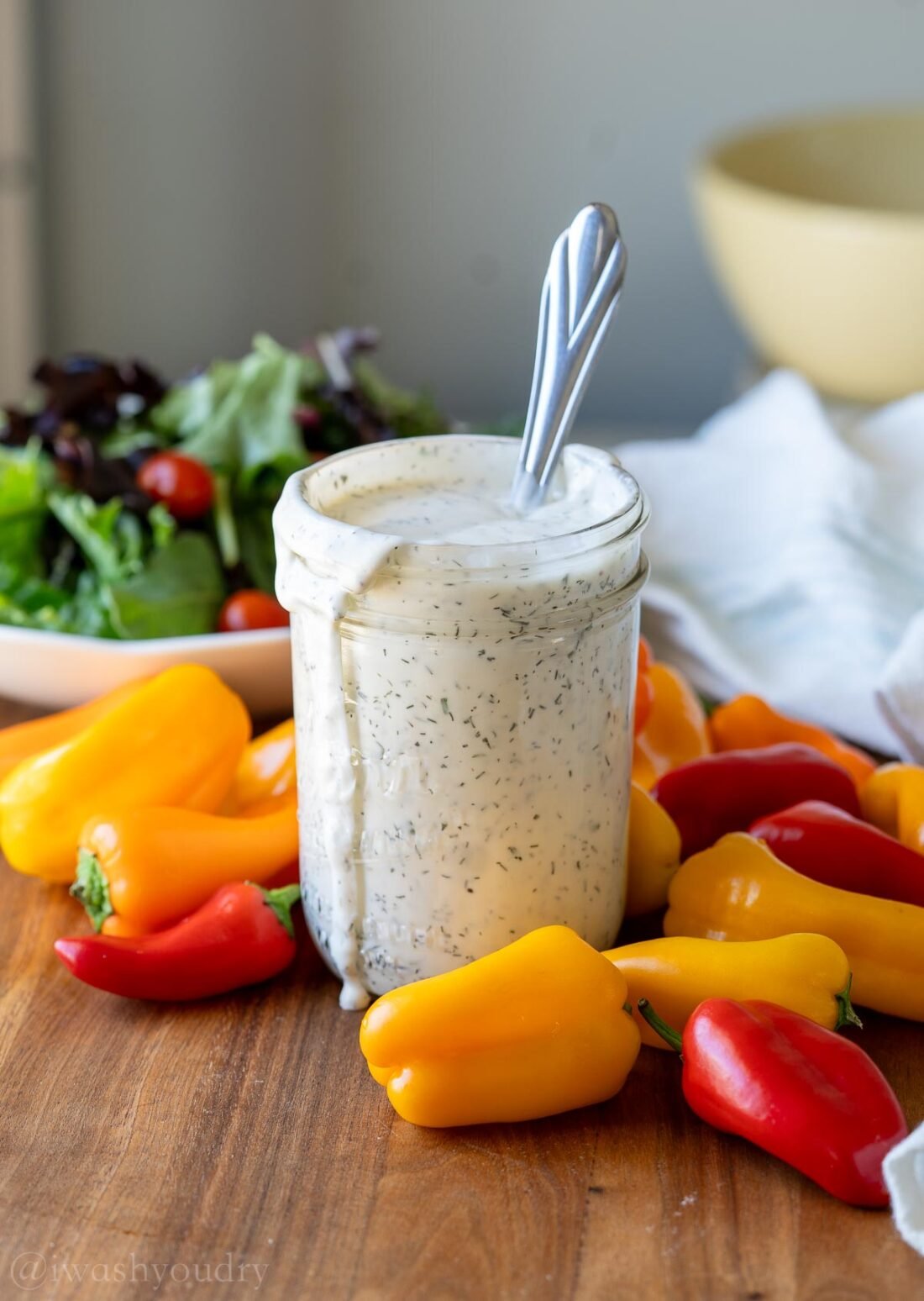 bottle of ranch dressing with spoon inside next to veggies and green salad.