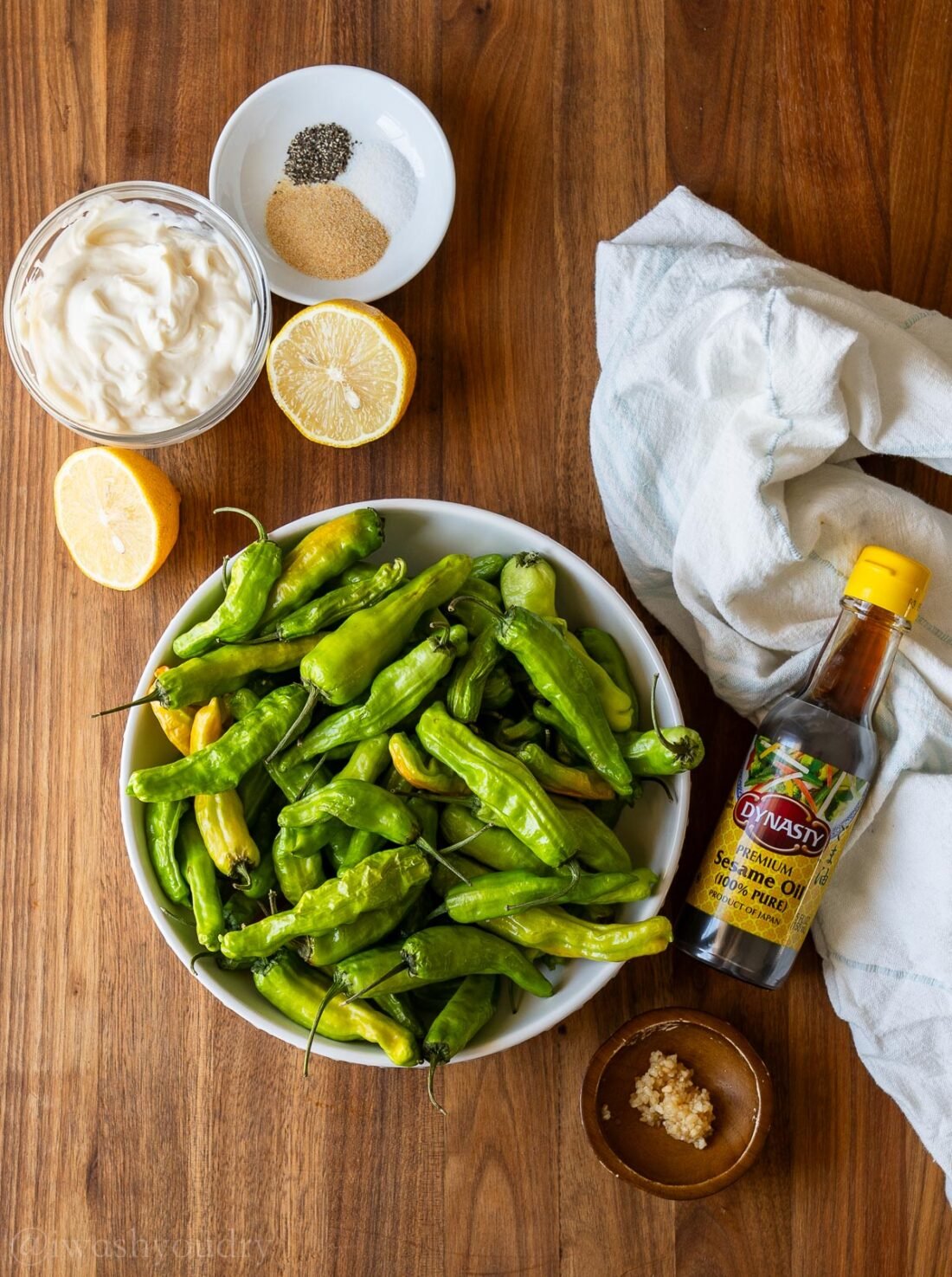 ingredients for shishito peppers with garlic aioli on a wooden surface with lemon wedges and sesame oil.