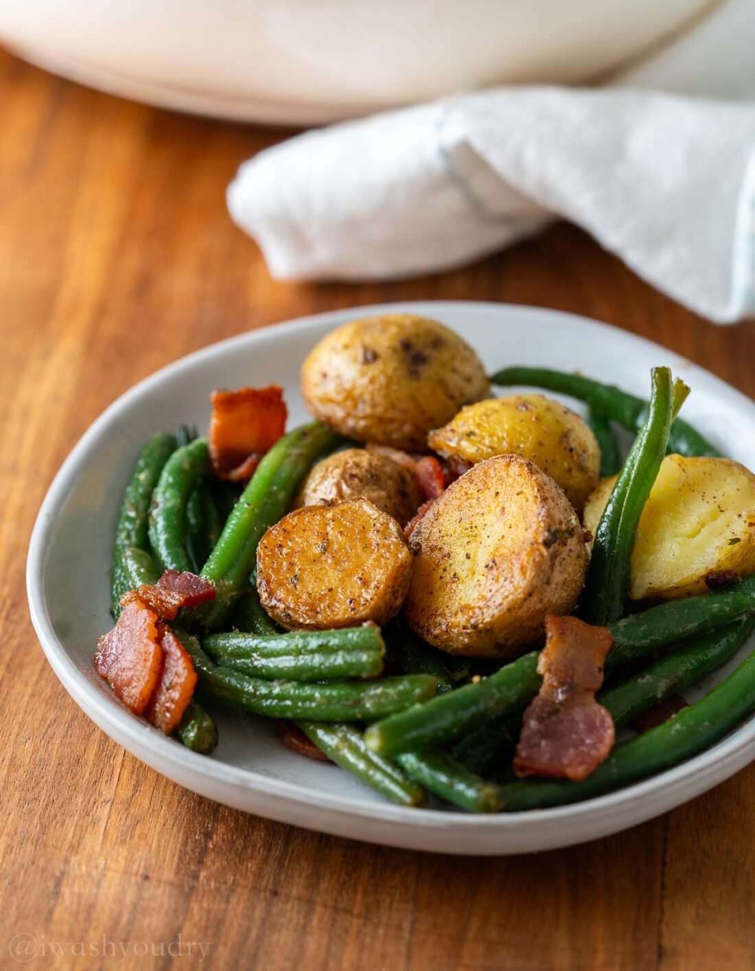 plate with green beans and bacon with crispy fried potatoes.