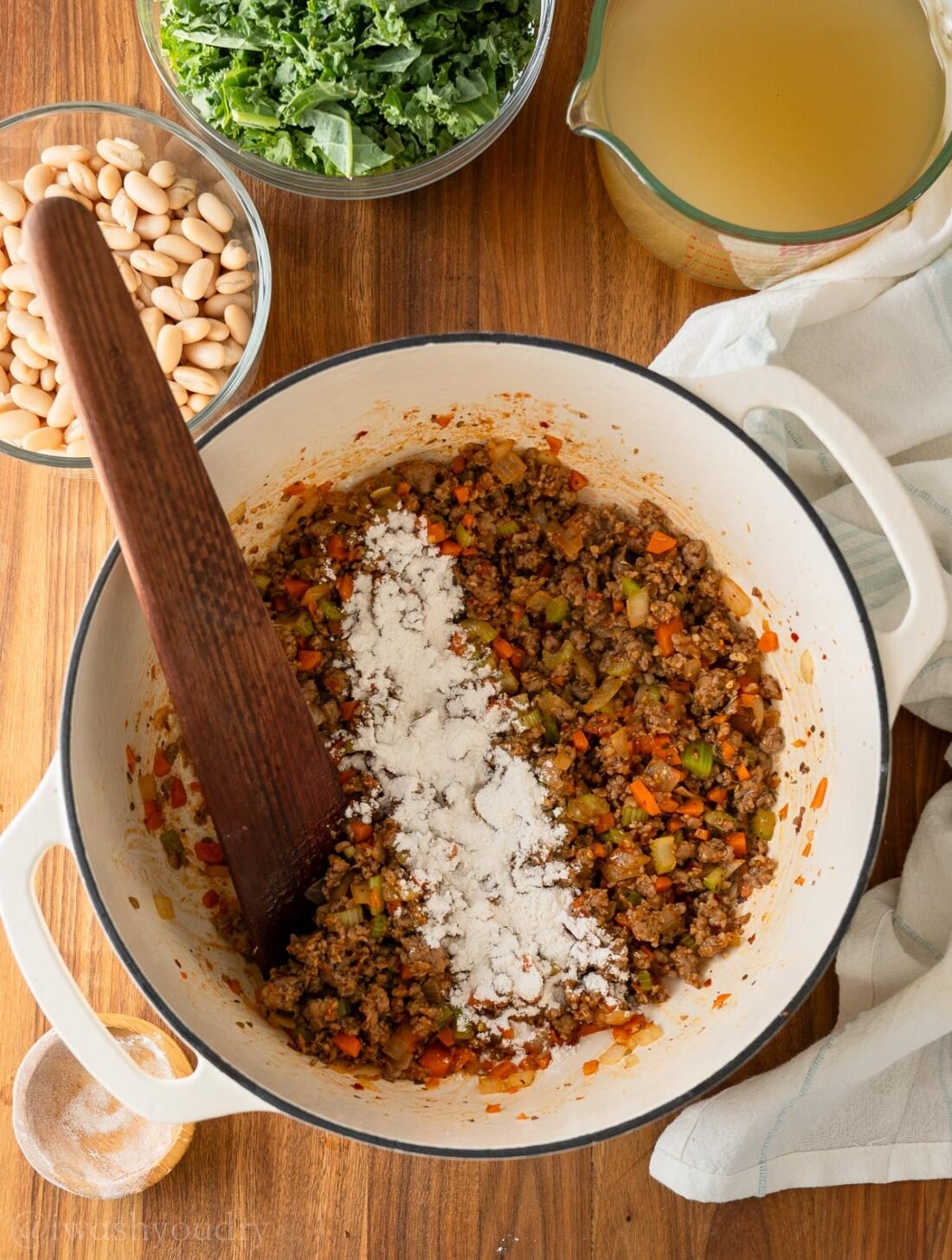 a blend of sausage and veggies in a white pot with flour sprinkled over the top.